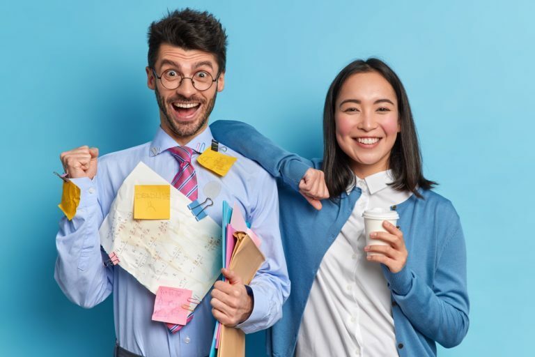 Successful businessman raises clenched fist and celebrates success at work female colleague stands n