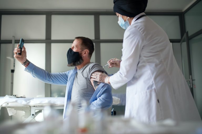 Man taking selfie when getting vacinated, coronavirus and vaccination concept
