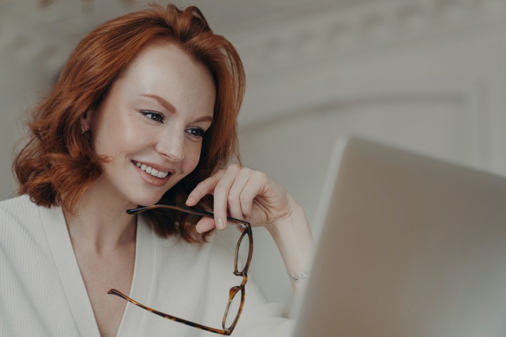 Ginger female web designer uses application on laptop