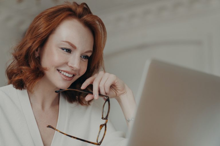 Ginger female web designer uses application on laptop
