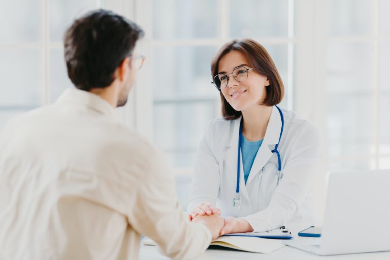 Confident female doctor holds hands of ill patient, persuades everything will be alright