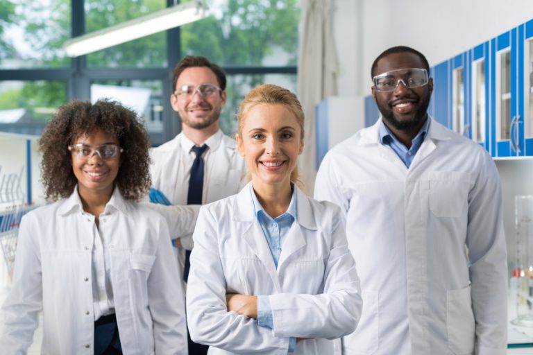 Smiling Group Of Scientists In Modern Laboratory With Female Leader, Mix Race Team Of Scientific