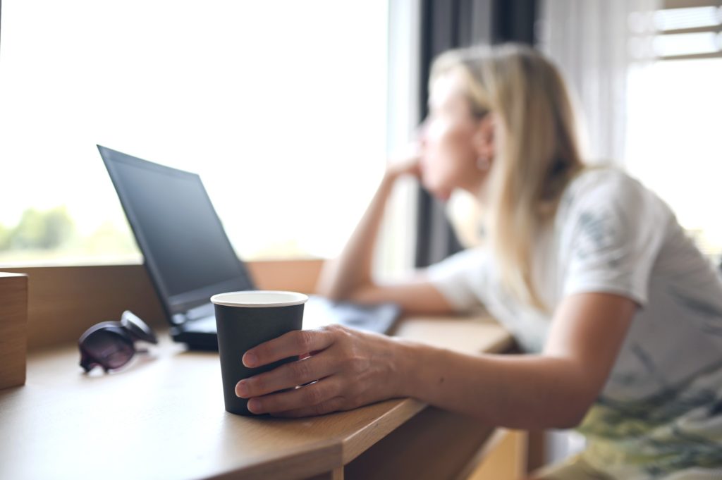 Sad unhappy blonde woman holding a paper cup of coffee and sitting and dreaming at the working desk
