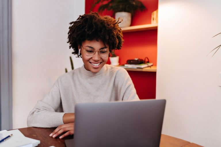 Woman in wireless headphones communicates via video link in laptop and posing in office with smile