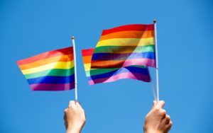 People holding and waving LGBT pride flags with blue sky background
